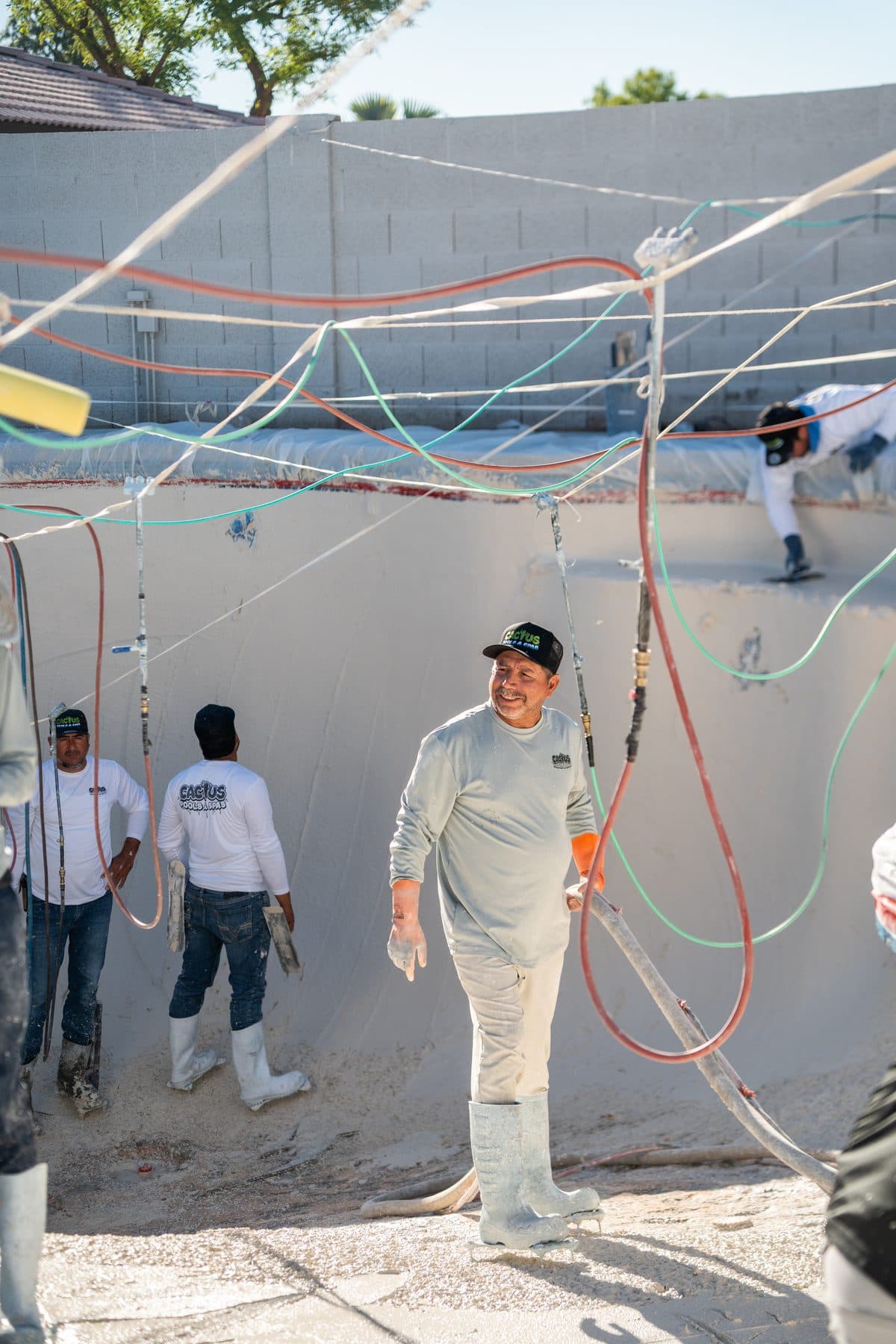 Crew members standing in an empty pool with hoses run overhead