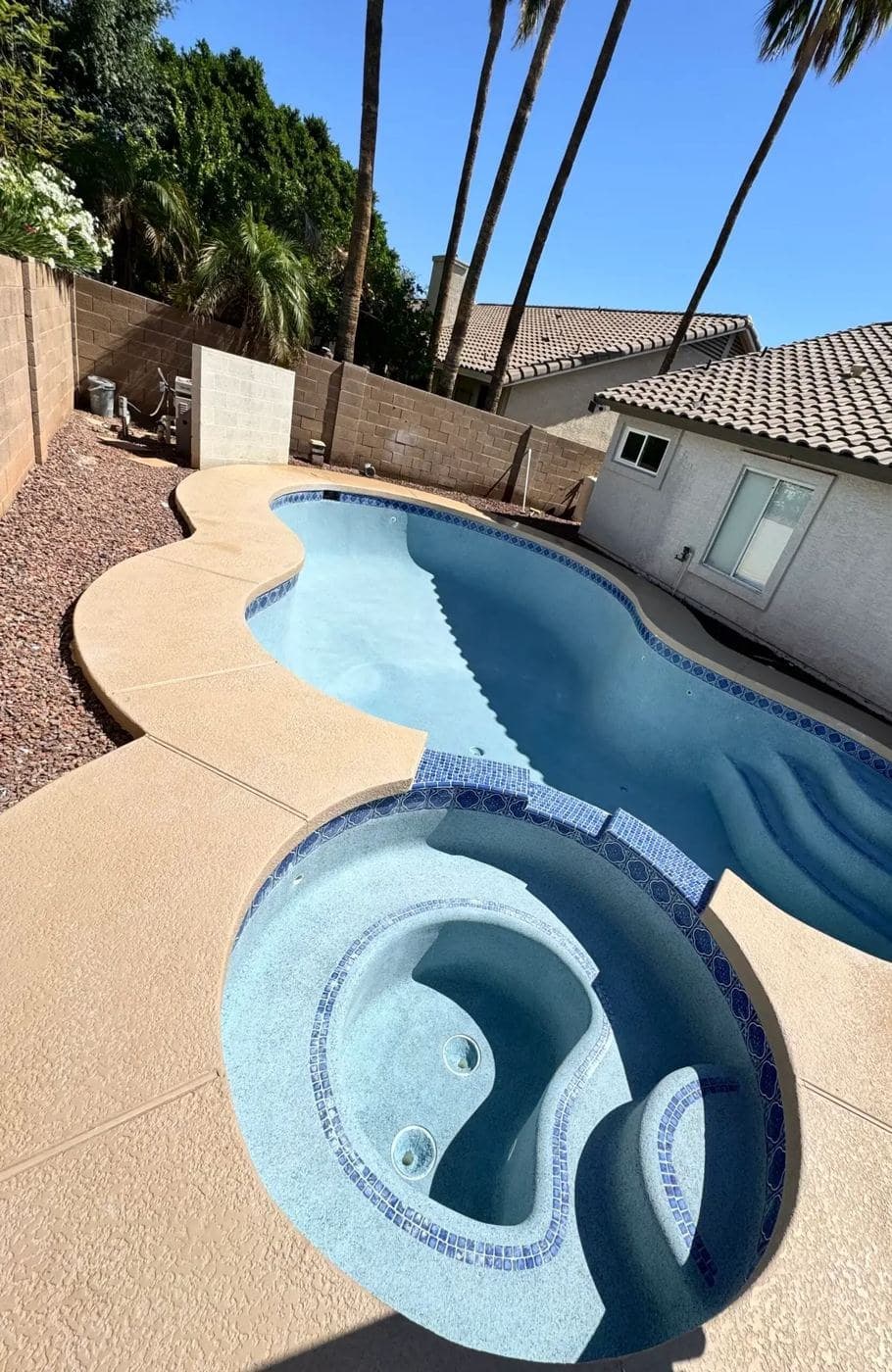 Curved pool with an attached round spa, blue tile trim and a tan deck
