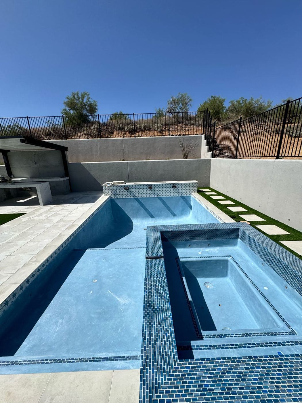 Empty long pool with a raised spa in blue glass tile and a new white deck