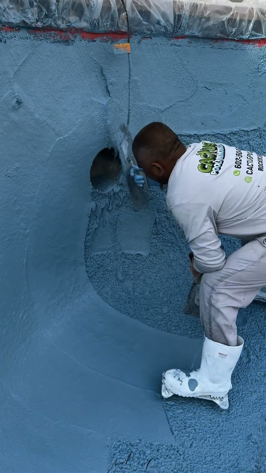 Crew member in a Cactus shirt troweling a new blue finish on a pool floor