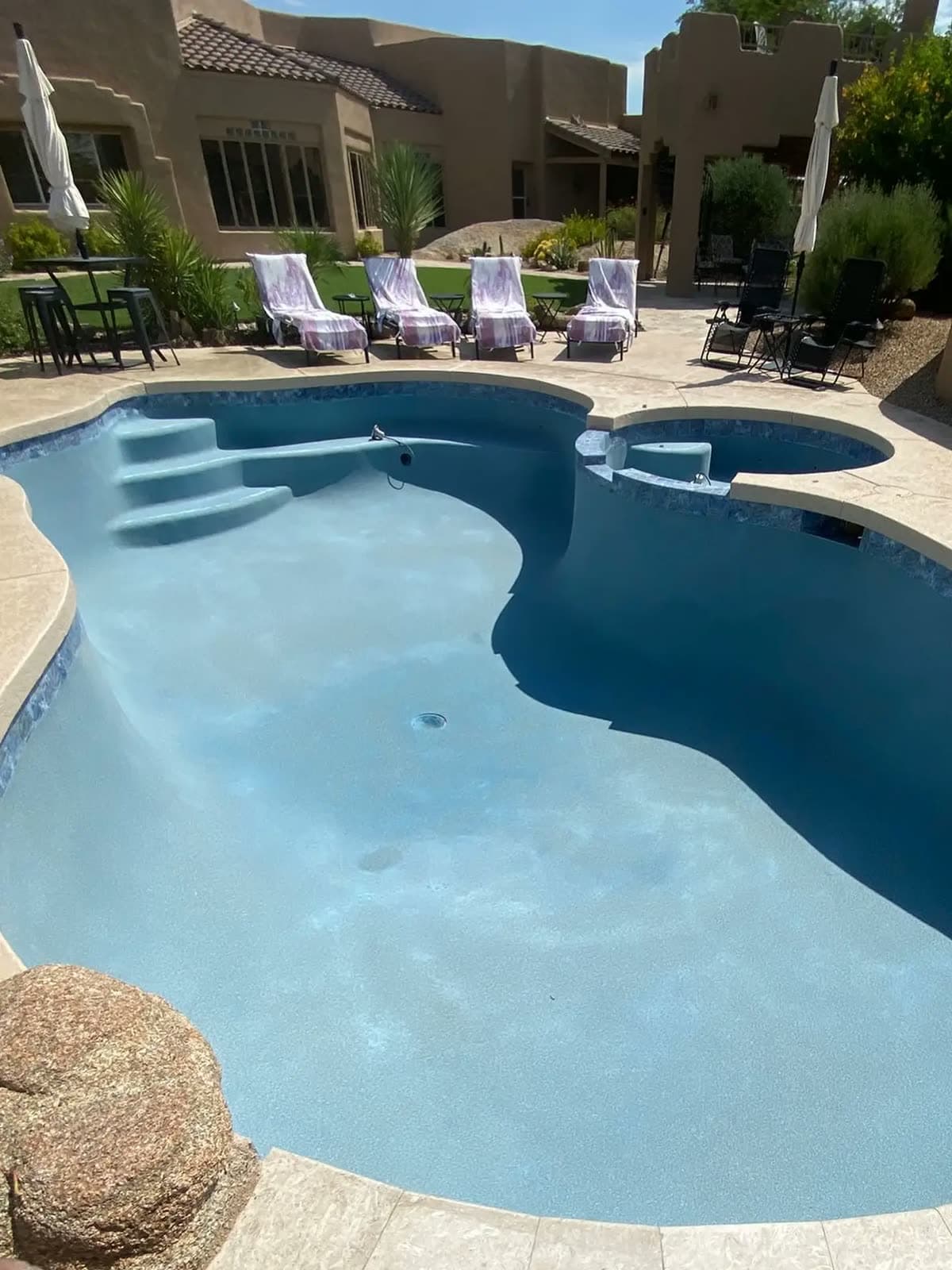 Empty curved pool and spa with a fresh light blue finish and a boulder