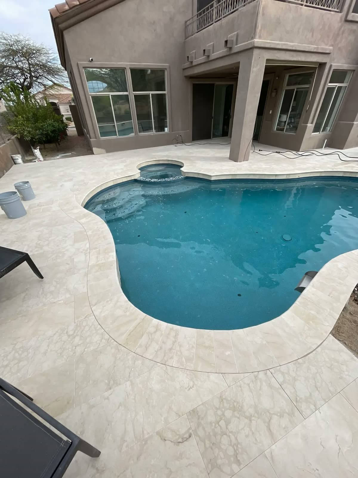 Curved pool and spa with a cream travertine deck behind a two story home