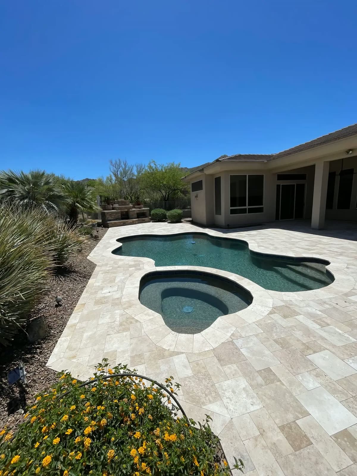 Curved pool and round spa with a travertine deck in a desert backyard
