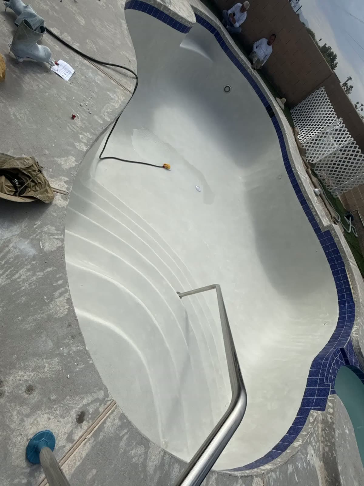 Empty pool with a new white plaster finish, blue tile and a handrail